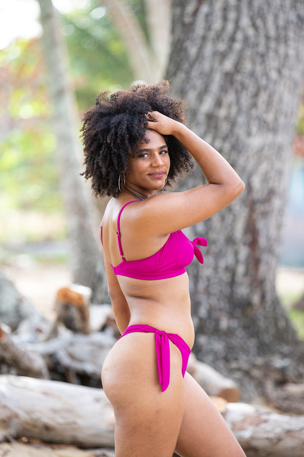 Marina Bralette in raspberry, side view of model in front of beach trees showing front tie, adjustable straps, and back hook closure.