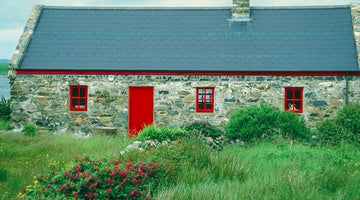 stone house in rural ireland with red windows and doors set behind green grass and wildflowers