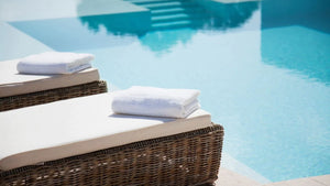 Wicker lounge chairs poolside with white towels and cushions 