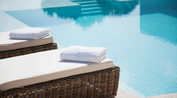 Wicker lounge chairs poolside with white towels and cushions 
