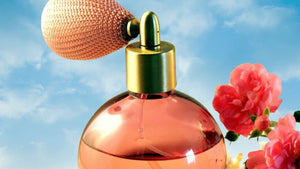 Amber colored perfume bottle against background of blue sky and pink flower