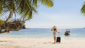 Woman on beach with suitcase by her side looking out on the ocean