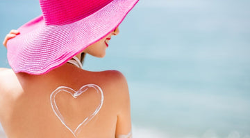 Woman on beach with large pink hat with heart shaped smear of suntan lotion