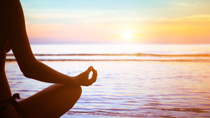 Woman on beach at sunset in lotus yoga pose