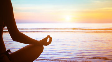 Woman on beach at sunset in lotus yoga pose