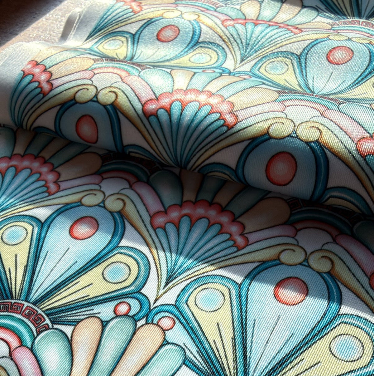 A close-up of a patterned fabric with a retro art deco design featuring teal, cream, pink, and yellow fan-like motifs.