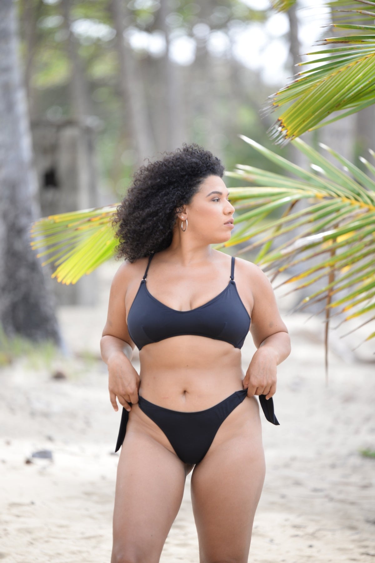 Hali Bikini Top in Black, front view on model, on beach, showing adjustable straps.