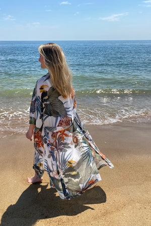 Model wearing Bambina Cardamom robe in tropical print standing on beach showing relaxed drape and vibrant print.