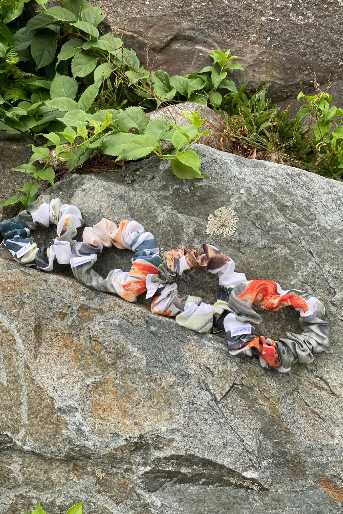 Multiple Cardamon Scrunchies placed on a rock with greenery showing print and round shape of gathered fabric.