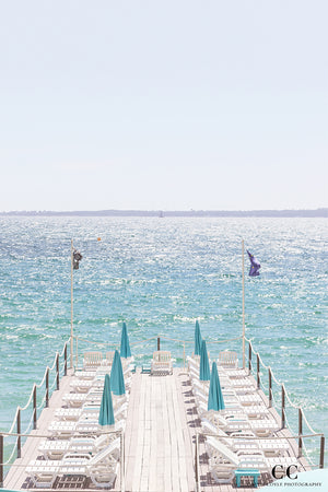 Pier with blue umbrellas extending into a calm body of water under a clear sky.