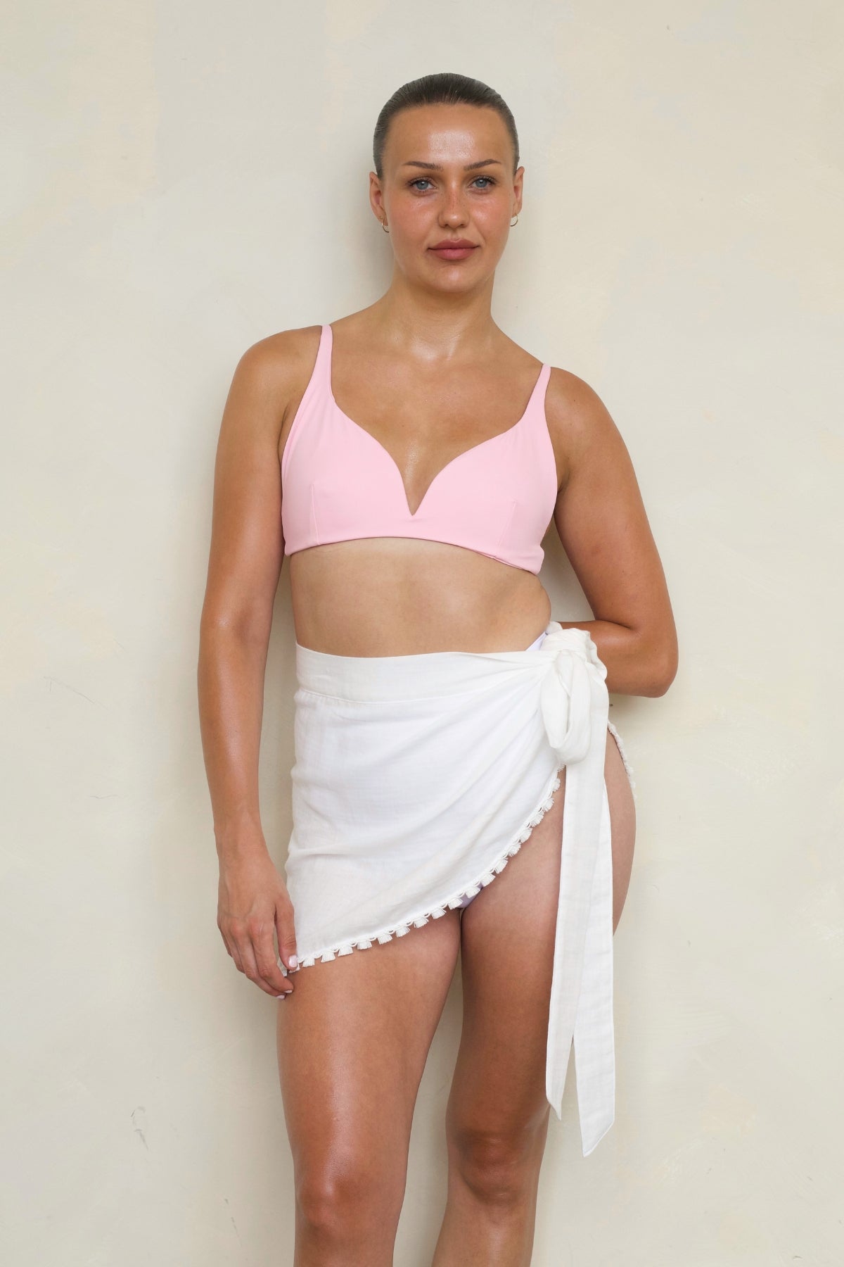 Savannah Mini Sarong in white front view on model wearing pink bikini top, showing wrap side-tie and tassel trim.