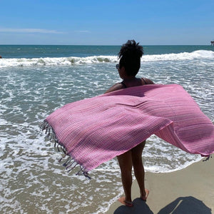 Person holding a pink towel on a beach with ocean waves in the background