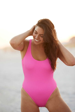 Woman on beach wearing a bright pink one piece bathing suit.