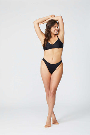 Woman in a black black bikini. Ring detail on strap, mid coverage bottom, high cut leg.