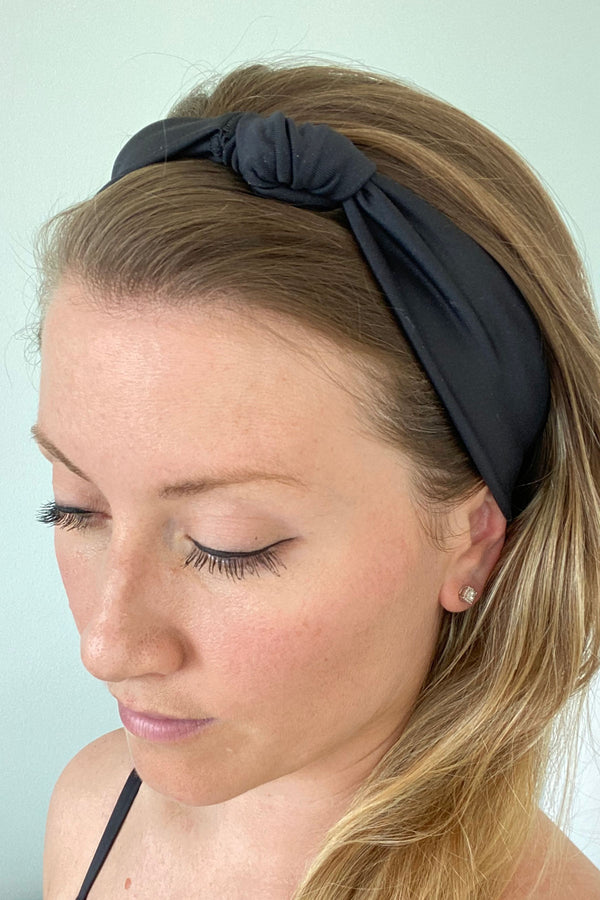 Woman wearing black headband with knot on top.