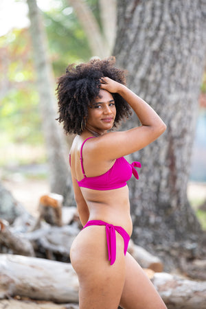 Serena Thong Bikini Bottom in raspberry, side view on model on beach, showing high cut leg and tie side.